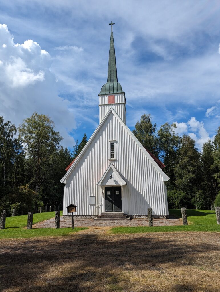Eine weiße Kirche mit einem sehr spitzen Kirchturm aus Kupfer, das von Grünspan bedeckt ist.