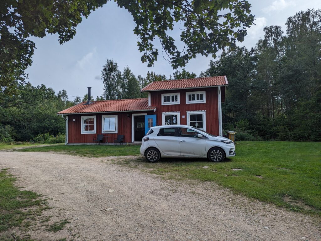 Die Zoe vor einem Ferienhaus im typischen Schwedenrot, dahinter Bäume.