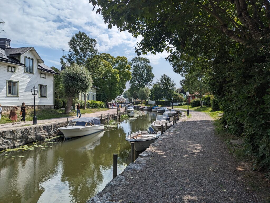 Kanal mit Booten, auf beiden Seiten Schotterwege und Häuser.