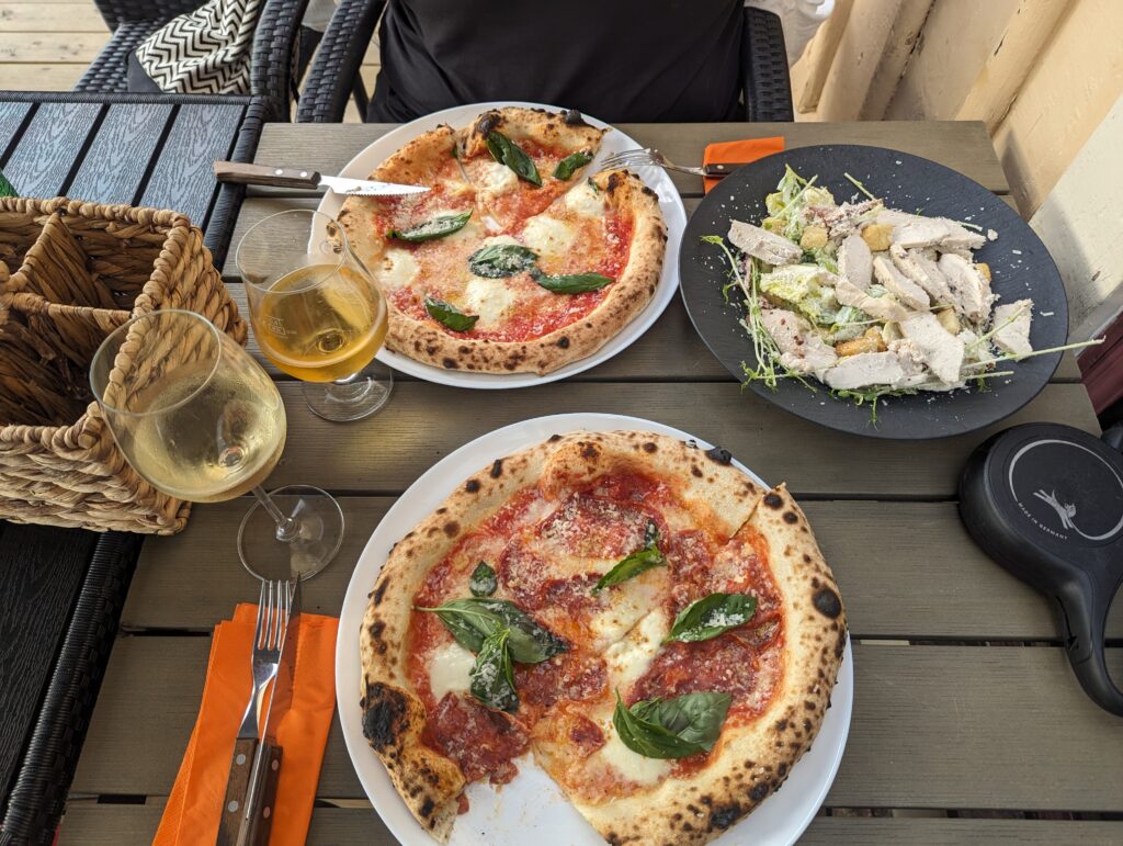 Ein Tisch mit zwei Tellern voll Pizza und einem mit Salat, ein Glas Wein und ein Glas Bier.