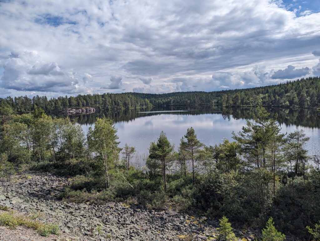 Blick auf einen See mit spiegelglatter Oberfläche, an den Rändern Wald, der sich im See spiegelt.