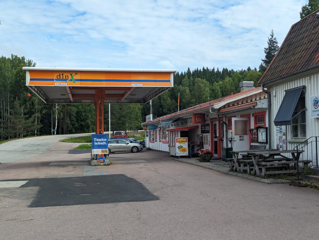 Links das Dach einer Tankstelle in orange, rechts davon ein einstöckiges Gebäude.
