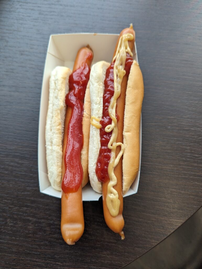 Zwei einfache Hotdogs in einer Papierschale, einer nur mit Ketchup, der andere mit Senf und Ketchup