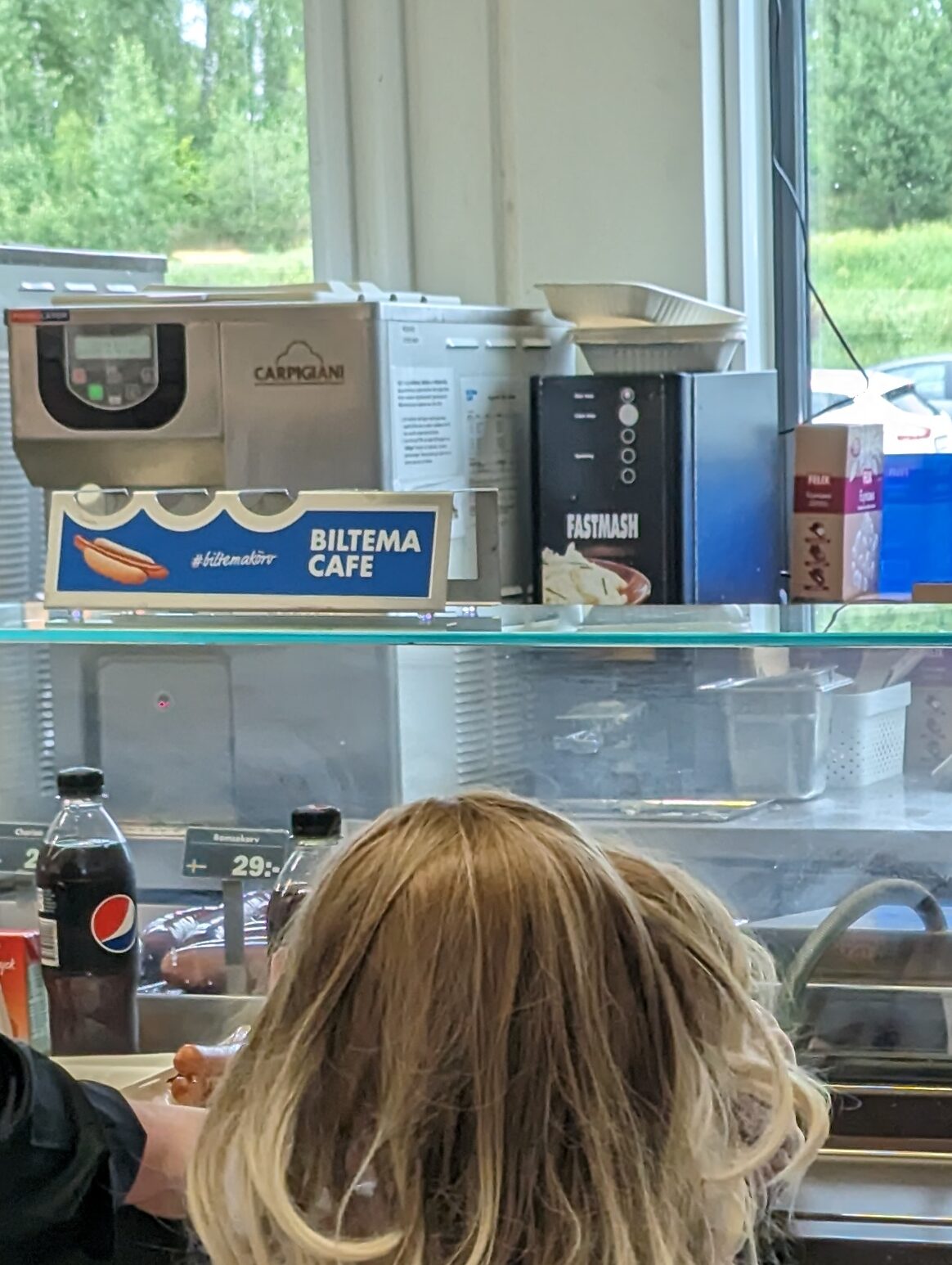 Ein Kind vor einer Theke eines Imbis, dahinter ist eine Maschine zu erkennen, die an einen Wasserspender erinnert, schwarze Front mit vier Knöpfen in Daumengröße, die Aufschrift FASTMASH