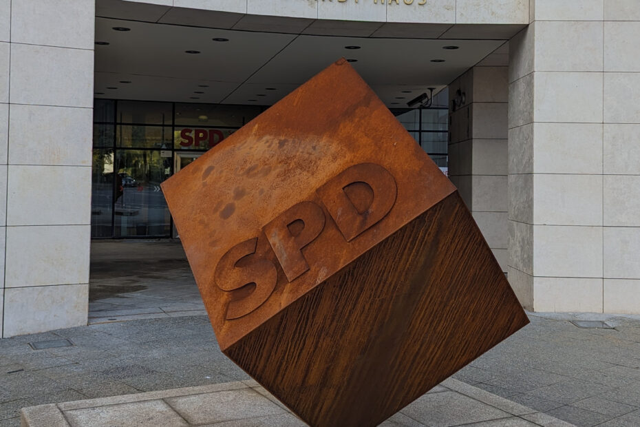 rostiger Würfel mit der Aufschrift SPD vor einem Haus aus hellgrauen Quadern, Über dem Eingang steht "Willy-Brandt-Haus"